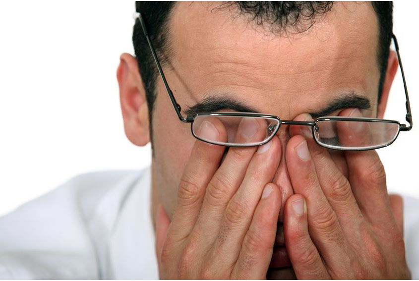 man wearing glasses, rubbing his eyes due to computer eye strain